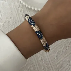 Detailed macro shot of vintage blue and white floral enamel bangle with gold metal trim