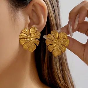Detail shot of vintage gold stainless steel monstera leaf earrings shown worn on ear.