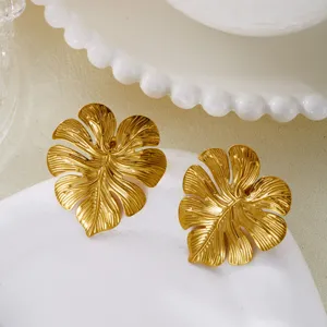 Detailed view of vintage gold monstera leaf earrings on elegant white ceramic plate