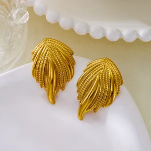 Macro detail view of vintage gold-plated feather earrings on a white ceramic plate.