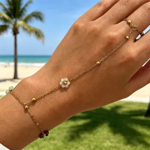 Bracciale a catena per mano dorata con fiore bianco e perline su sfondo spiaggia