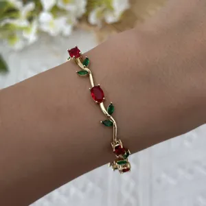 Detailed view of a gold-plated vine bracelet with red and green crystals on a wrist.