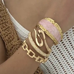 Detailed macro view of stacked gold tone bracelets with pink enamel and floral engraving