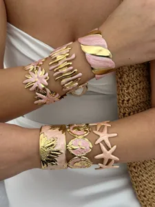 Detail von vergoldeten Manschettenarmbändern aus Edelstahl mit rosa Emaille und Seestern
