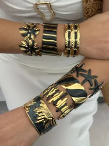 Detailansicht von vergoldeten Edelstahl-Armreifen mit Emaille-Sternen und Blumen.