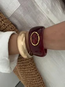 Détail d'un jonc en résine bohème rouge foncé et d'un bracelet doré mat portés au poignet