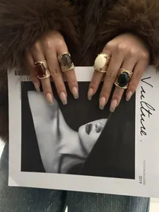 Close-up of four chunky resin rings in bohemian hip-hop style worn on hands holding a magazine