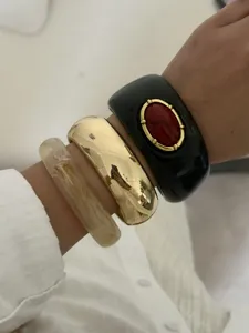 Set aus Vintage-Resin- und goldfarbenen Armreifen mit rotem Stein-Inlay am Handgelenk.