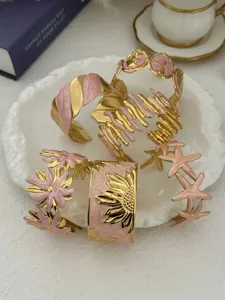 Detailansicht vergoldeter Edelstahlmanschetten mit rosa Emaille-Blumen-Designs.