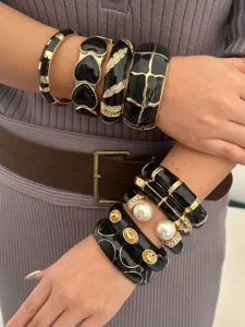 Detailweergave van gestapelde vintage zwarte emaille en gouden legering armbanden op de arm.