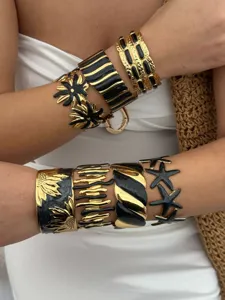 Makroaufnahme von gold-schwarzen Edelstahl-Armreifen mit Seestern- und Blumenmuster.