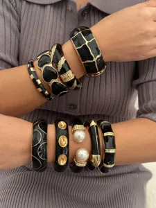 Detailweergave van vintage emaille armbanden gestapeld op armen, goud en zwart lak.