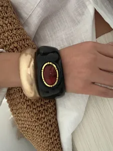 Gros plan détaillé de gros bracelets bohèmes en résine noire et or sur un bras en lin