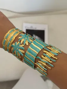 Detail showing a stack of gold and turquoise enamel cuff bracelets on a wrist.