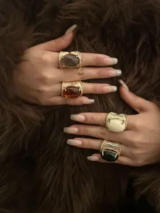 Detailed view of four chunky gold rings with resin stones on a brown faux fur background