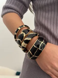 Gedetailleerd overzicht van gestapelde vintage zwart geëmailleerde gouden armbanden.