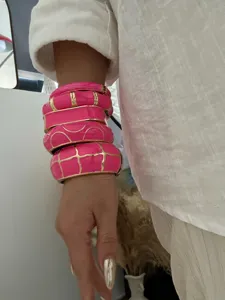 Macro view of bold hot pink enamel bangles set with gold geometric patterns on a wrist.
