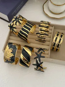 Detailansicht goldener und schwarzer Emaille-Armreifen mit Seestern- und Blumenmustern.