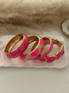 Detailed view of four vibrant pink enamel bangles with gold-plated geometric patterns