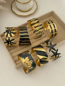 Sortiment an gold-schwarzen Emaille-Armreifen aus Edelstahl mit Seestern- und Blumenmustern.