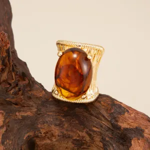 Macro detail of a chunky gold-tone ring featuring a large oval amber resin stone