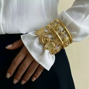 Dettaglio del bracciale rigido dorato con motivi marini in acciaio inossidabile sul polso.