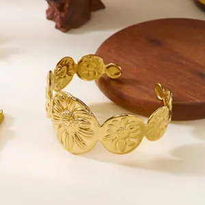 Dettaglio di un bracciale a polsino in acciaio dorato con motivo a girasole a rilievo