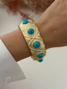 Detailed view of an ornate gold-tone alloy bangle featuring vibrant turquoise stones on a wrist