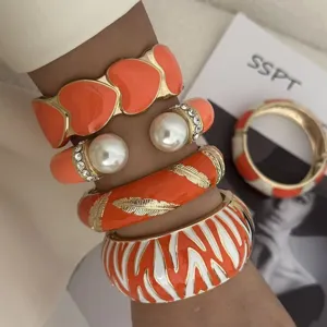 Stapel lebhaft orangefarbener und weißer Zebra-Emaille-Armreifen und Perlenarmbänder