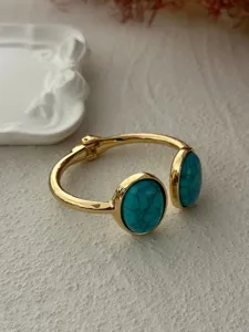 Detailed view of an elegant gold-toned bangle featuring dual oval turquoise stones