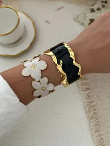 Detailansicht von Emaille-Blumen und schwarzen Wellen-Gold-Armreifen am Handgelenk