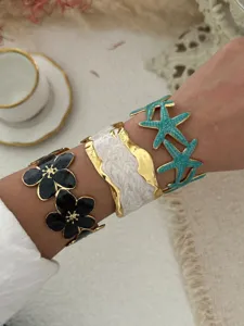 Drei verschiedene Emaille-Armreifen mit Blumen- und Seesternmotiven am Handgelenk
