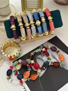 Detailweergave van kleurrijke macaron kralenarmbanden met gouden accenten op een standaard