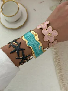 Detailansicht der vergoldeten Emaille-Armreifen mit Blumen- und Seestern-Motiven.