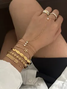 Macro view of multiple stacked gold bracelets and flower zircon rings on a model's wrist.