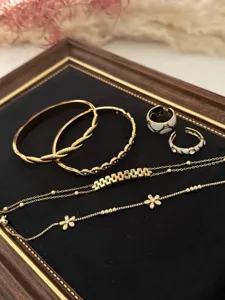 Close-up of gold-plated jewelry collection featuring flower bracelets and elegant rings on black velvet