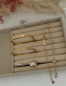 Detailed view of dainty gold bracelets and flower zircon rings displayed in a velvet tray