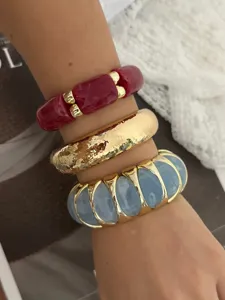 Nahaufnahme von gestapelten bunten, breiten Stretch-Armbändern in Rot, Gold und Blau