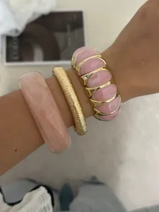 Detailansicht von stilvollen rosafarbenen Harz- und goldfarbenen elastischen Armbändern.
