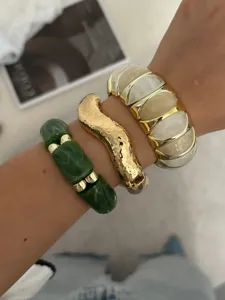 Detailansicht geschichteter breiter Mode-Armbänder in Gold, Grün und Weiß am Handgelenk.