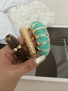 Detail von drei stylischen elastischen Armbändern in Gold, Türkis und Dunkelbraun.