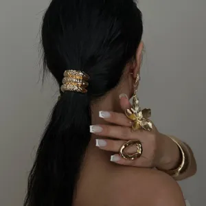 Elegante gouden gehamerde sieradenset met armband, ring en grote bloemenoorbellen.