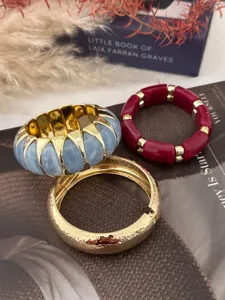 Detailansicht von bunten Stretch-Armbändern und einem gehämmerten goldenen Armreif.
