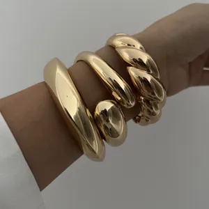 Close-up van grove goudkleurige metalen armbanden met gladde en gedraaide ontwerpen.