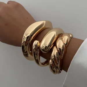 Close-up van meerdere grove goudkleurige metalen armbanden met gladde en gedraaide ontwerpen.