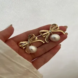 Nahaufnahme von eleganten goldenen Schleifenohrringen mit großen Perlenanhängern