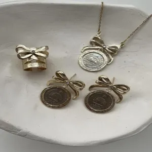 Vintage-Schmuckset mit goldener Schleife und Münzmedaillon in weißer Keramikschale.