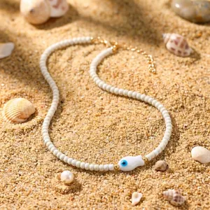 Detailaufnahme einer böhmischen weißen Perlenkette mit Keramikfisch auf Sandstrand