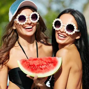 Dos mujeres felices con elegantes gafas de sol de margaritas blancas en una playa de verano