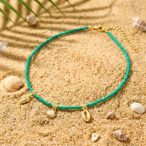 Bohemian Türkis Perlenkette mit goldenen Muschelanhängern auf Sandstrand-Hintergrund.